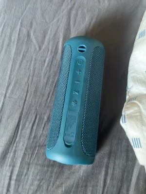 Blå JBL trådlös högtalare - Snygg blå trådlös högtalare från JBL med cylinderformad design. Högtalaren har gummerade knappar för volym, ström och Bluetooth samt robust tygmaterial runt om. Perfekt för att ta med sig och spela musik trådlöst via Bluetooth.