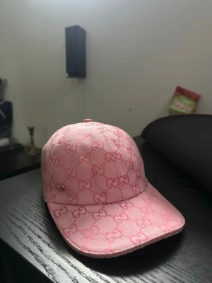Rosa Gucci keps med GG-mönster - Säljer en snygg rosa keps från Gucci med det klassiska GG-mönstret över hela kepsen. Kepsen är i storlek M (58 cm) och har en böjd skärm. Materialet är canvas med insida i ljus textil. Perfekt för dig som vill sticka ut med en lyxig accessoar. Box och allt där med finns med 