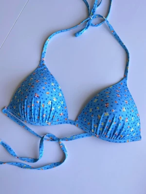Blå trekantsbikini med blommor, storlek L - Söt blå trekantsbikini med små blommiga detaljer. Knytband i nacken och i ryggen. True to size. 📏 Storlek: L