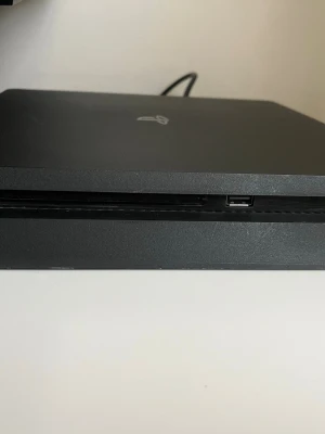 PlayStation 4 Slim svart konsol - Säljer en svart PlayStation 4 Slim från Sony. Konsolen har en stilren, matt finish och är tillverkad i plast. Den har USB-portar fram och bak, nätverksuttag samt HDMI-utgång. Perfekt för gaming och streaming. Kommer med 8 spel, om det är strul med att få igång spelen, öppna då övre delen och rengör med antingen tryckluft på burk eller blås