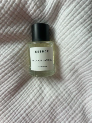 ESSNCE Delicate Jasmine parfym - Använd parfym! Minimalistisk parfymflaska från ESSNCE med doften Delicate Jasmine. Flaskan är genomskinlig i glas med svart cylinderformad kork och vit etikett med svart text. Eau de Parfum som ger en fräsch och blommig känsla. Används ej då lukten inte passar mig. Använd fåtal gånger, syns på bild två. Ska dofta likt Giorgio Armanis My Way.  Kostar 360kr nypris och rymmer 50 ml