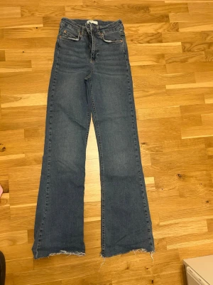 Gina Trickot bootcut jeans storlek s - Snygga blå bootcut jeans med hög midja och råa, fransiga benslut. Klassisk femficksmodell med dragkedja och knapp. Perfekta för en avslappnad och trendig look.