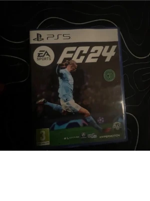 EA Sports FC24 till PS5 - EA Sports FC24 till PlayStation 5, fotbollsspel med realistisk grafik och uppdaterade lag. Omslaget har en spelare i ljusblå matchställ. Perfekt för dig som gillar sportspel och vill spela med vänner på PS5.