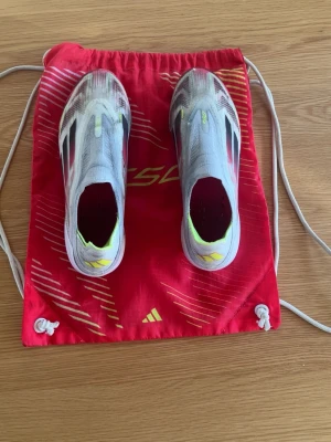 Adidas X Speedflow+ fotbollsskor - Säljer ett par Adidas f50 fotbollsskor i vitt med svarta och gula detaljer. Skicket är otroligt bra och säljer endast då skorna är för små. Skorna har en strömlinjeformad design utan snörning och ovandel i syntetmaterial. Sulan har färgskiftningar i rött, gult och vitt. Perfekta för snabba spelare som vill sticka ut på planen. 