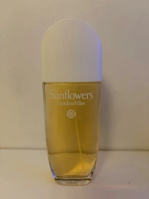 Sunflowers Golden Vibe parfym - Fräsch parfym från Elizabeth Arden, Sunflowers Golden Vibe. Flaskan är genomskinlig med guldfärgad vätska och har ett stilrent vitt lock. Perfekt för dig som gillar blommiga och fruktiga dofter.