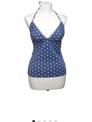 Blåprickig tankini från Esprit - Snygg blå tankini från Esprit med vita prickar och halterneck-knäppning. Toppen har en feminin v-ringning och är tillverkad i ett stretchigt material som passar perfekt för strandhäng och pooldagar.