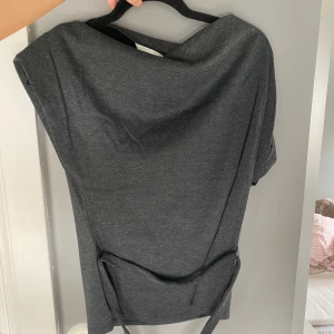 Mörkgrå omlottkavaj med bälte - Stilren mörkgrå omlottkavaj med bälte i midjan. Kavajen har en klassisk krage och ett diskret fiskbensmönster. Perfekt för dig som vill ha en modern och elegant look.