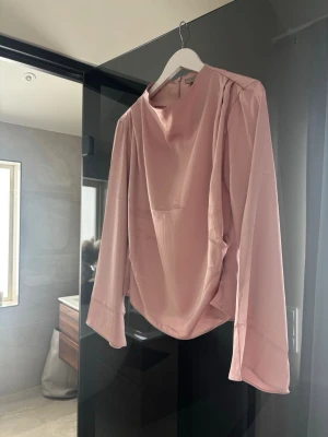 Ljusrosa satinblus med vida ärmar - Supersnygg ljusrosa blus i satinliknande material med rund halsringning och långa, vida ärmar. Blusen har en avslappnad passform och dragkedja i ryggen. 