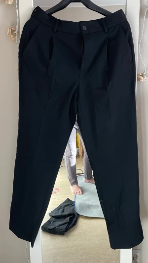 Svarta MNG  kostymbyxor med pressveck - Snygga svarta MNG kostymbyxor med klassiskt pressveck och hällor för skärp. Byxorna har snedställda fickor fram och passpoalfickor bak. Rak passform och stängs med knapp och dragkedja. Perfekta för en stilren look.nypris har kostat 800kr