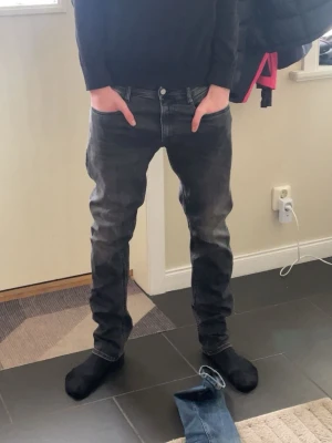 Svarta slim fit jeans med tvättad look - Säljer ett par svarta slim fit jeans med snygg tvättad effekt och klassiska fem fickor. Jeansen har normal midja och raka ben. Passar perfekt till en avslappnad stil och är gjorda i ett mjukt denimtyg för extra komfort.