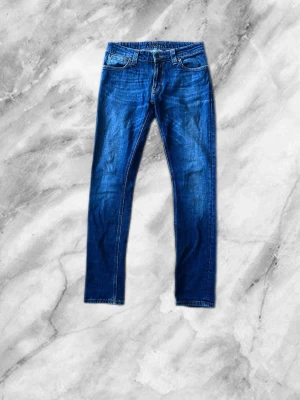 Blå skinny jeans från Crocker - Säljer ett par klassiska blå skinny jeans från Crocker med fem fickor och normal midja. Jeansen har snygga slitningar och kontrastsömmar, perfekta till vardagslooken. Materialet är stretchigt denim som sitter tajt och bekvämt.