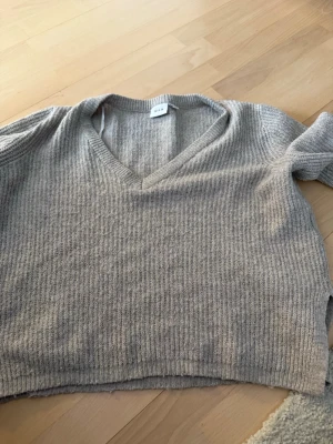 Beige stickad tröja från Vila - Mysig beige stickad tröja från Vila med v-ringning och ribbad struktur. Tröjan har långa ärmar och en avslappnad passform, perfekt att slänga på sig till jeans eller kjol. Materialet känns mjukt och bekvämt mot huden.