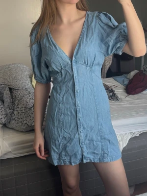 Blå kort jeansklänning Monki - Söt blå kort klänning från Asos design i jeans med v-ringning, puffärmar och knappar framtill. 