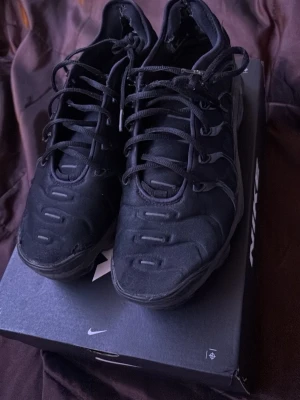 Svarta Nike sneakers  - Säljer ett par helsvarta Nike sneakers med cool design och detaljerad snörning. Skorna har en sportig look med robust sula och ovandel i textil och syntet. Inne i skorna har de hål, o båda skorna är punkterade, så därför säljs de för ett mindre pris. Först till kvarn!