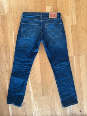 Levi's 511 - Snygga blå jeans från Levi's i klassisk femficksmodell med smal passform. Jeansen har en mörk tvätt med lätt slitning framtill och bakfickor med den ikoniska Levi's-sömmen. Tillverkade i bomull med en liten stretch för extra komfort.