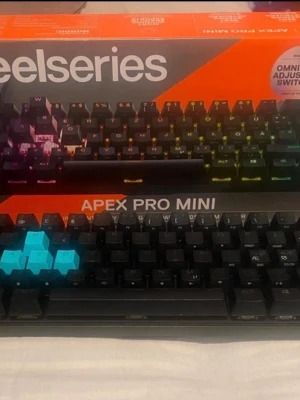 SteelSeries Apex Pro Mini tangentbord - SteelSeries Apex Pro Mini är ett kompakt mekaniskt tangentbord med RGB-belysning och svarta tangenter. Några tangenter är utbytta till ljusblå för gaming. Tangentbordet har OmniPoint justerbara switchar och levereras i originalförpackning.
