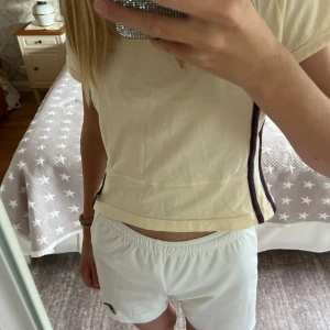 Vita Adidas shorts - Snygga vita Adidas shorts med climalite-teknologi som håller dig sval. De har elastisk midja för skön passform och är tillverkade i lätt polyester. Perfekta för sport eller chill, med diskret Adidas-logga på benet. Klassisk och enkel design som funkar till allt. Säljer även träningströjan jag har på första bilden (se separat annons, du kan få köpa båda två för ett bättre pris). Hör av er om frågor!❤️