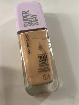 Maybelline Super Stay Foundation 129 - Maybelline Super Stay 30H foundation i nyansen 129. Kommer i en rektangulär glasflaska med lila plastlock. Ger en matt finish och har en ljus beige ton. Perfekt för dig som vill ha en täckande bas som håller länge.