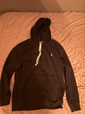 Svart hoodie från Polo Ralph Lauren - Säljer en svart hoodie från Polo Ralph, med vit dragsko i huvan och klassisk känguruficka framtill. Liten broderad logga wanna topless på bröstet. Perfekt oversized fit och mjukt material som känns riktigt skönt mot huden.