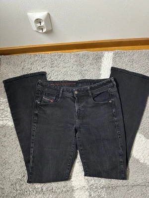 Svarta bootcut jeans från Diesel - Säljer ett par svarta bootcut jeans från Diesel med klassisk femficksdesign och knappgylf. Jeansen har en diskret tvättad look och är tillverkade i mjukt denimtyg. Perfekta för dig som gillar en avslappnad men snygg stil.