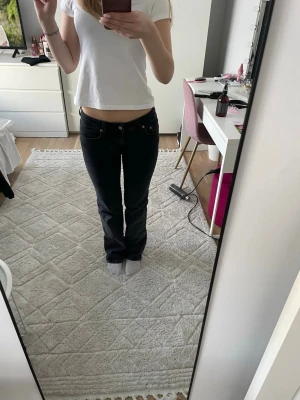 Svarta bootcut jeans med låg midja - Säljer ett par svarta bootcut jeans med låg midja och klassisk femficksmodell. Jeansen har en smal passform upptill och lätt utsvängda ben. Perfekta till en avslappnad och trendig stil.