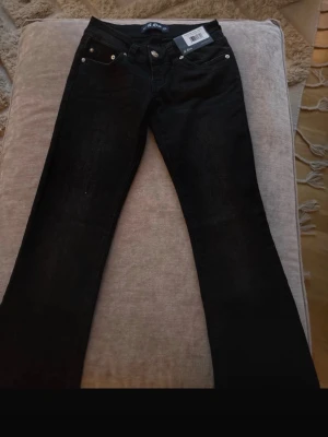 Svarta bootcut jeans från Lee - Säljer ett par svarta jeans från Lee med klassisk bootcut passform. Jeansen har fem fickor, silverfärgade nitar och Lee-logga på bakfickan. Tillverkade i kraftig denim som ger en snygg siluett och passar perfekt till sneakers eller boots.
