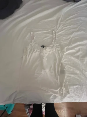 Vit linnetopp med spetsdetaljer -  Säljer 2 st linnen. Supersöt vit linnetopp från New yorker med tunna axelband och fina spetsdetaljer längs urringningen. Materialet känns mjukt och lätt mot huden.