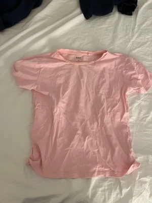 Ljusrosa t-shirt från 157 - En enkel ljusrosa t-shirt från 157 med rund hals och korta ärmar. T-shirten är gjord i mjuk bomull och har en klassisk passform som är lätt att matcha med jeans eller shorts. Perfekt för dig som gillar basic och stilrena plagg.