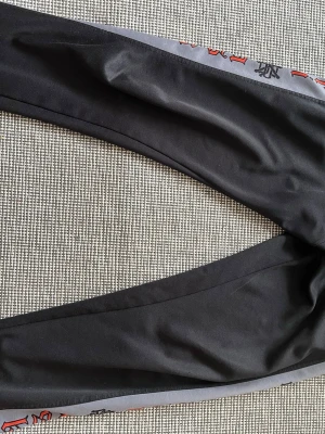 Svarta leggings med grått tryck - Säljer ett par svarta Askari byxor som är äldre och inte går att köpa längre. Finns lite defekter som dragkedjan på vänster sida i fickan är trasig men höger funkar. Dom är extremt snygga och sköna men dom säljs med en liten tår i ögat 