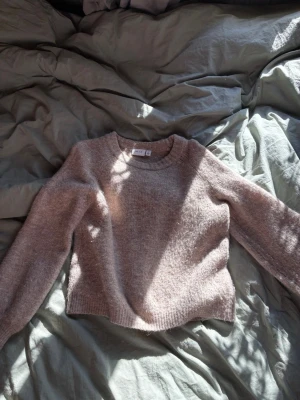 Beige stickad tröja från vila - Mysig beige stickad tröja från vila med rund halsringning och långa ärmar. Tröjan har en mjuk, luddig yta och ribbstickade muddar vid ärmslut och nederkant. Perfekt för lager på lager och enkel att matcha med jeans eller kjol.