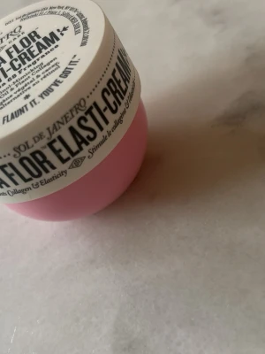 Sol de Janeiro Beija Flor Elasti-Cream - Beija Flor Elasti-Cream från Sol de Janeiro är en kroppskräm med Cheirosa 68-doft, retinol-liknande ingredienser, cacayolja och växtbaserat kollagen. Burken är rosa med vitt lock och svart text. Perfekt för dig som vill boosta hudens elasticitet.