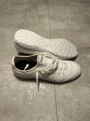 Vita Puma King inneskor - Säljer ett par stilrena vita Puma King inneskor med klassisk låg profil och snörning. Skorna har en ovandel i syntetmaterial med struktur för bättre bollkontroll och en slitstark yttersula med greppmönster, perfekt för användning på inomhusplan. Storlek: 43. Använt ett fåtal gånger men i bra skick.                                                           Hör av er vid frågor! Skickas snabbt o välpackat!