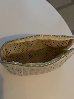 Prickig necessär i tyg med dragkedja - Söt necessär i vit tyg med små svarta prickar och quiltad struktur. Invändigt är den fodrad med beige tyg och svarta prickar. Stängs med dragkedja upptill och passar perfekt för smink eller små skönhetsprylar.