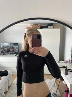 Svart croppad långärmad topp 157 - Säljer en svart croppad långärmad topp från 157 med logga på bröstet. Toppens material är syntet och polyester, perfekt för träning eller chill. Slim fit och enkel design som är lätt att matcha med jeans eller tights.