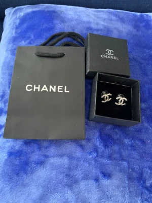 Chanel örhängen CC - Säljer ett par ikoniska Chanel örhängen i silverfärg med gnistrande strass-stenar och CC loggan. Örhängena har den klassiska CC-loggan och kommer i  ask och påse. 