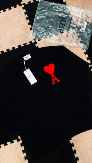 Svart stickad tröja från Ami Paris - Svart stickad tröja från Ami Paris med ett stort rött hjärta och bokstaven A broderat på bröstet. Tröjan har rund hals, ribbade muddar och lång ärm. Perfekt för dig som gillar stilrena detaljer med en twist.
