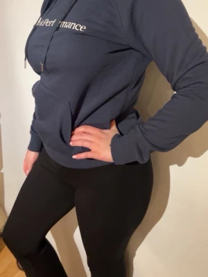 Mörkblå Peak Performance hoodie - Säljer en mörkblå hoodie från Peak Performance med vit logotyp på bröstet. Tröjan har huva med dragsko och en stor magficka. Materialet är mjukt och bekvämt, perfekt för chill dagar. Långa ärmar och ribbade muddar ger en snygg passform.