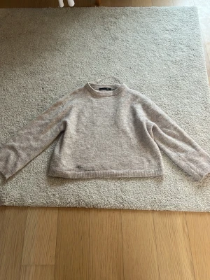 Beige stickad tröja från Lager 157 - Mysig beige stickad tröja från Lager 157 med rund halsringning och långa ärmar. Tröjan har en rak passform och ribbstickade muddar vid ärmslut och nederkant. Perfekt för lager-på-lager och enkel att matcha med jeans eller kjol.