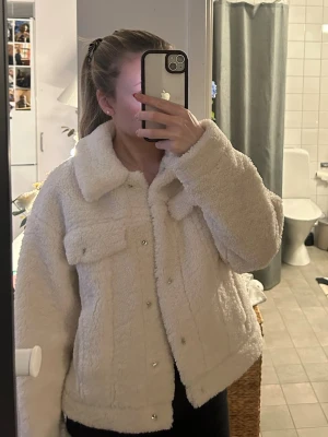 Vit teddyjacka från NA-KD - Mysig vit teddyjacka från NA-KD med stora bröstfickor, bred krage och knappar framtill. Jackan har en boxy passform och är gjord i fluffigt teddy-material 