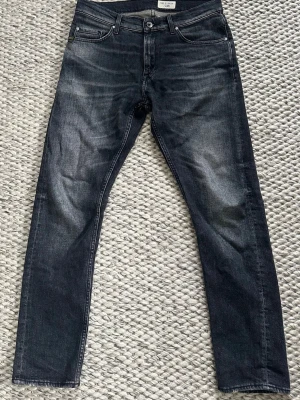 Mörkgrå slim fit jeans från tiger of sweden  - Mörkgrå slim fit jeans från tiger of sweden med modellen "Pistolero" samt diskreta slitningar på låten. Jeansen har knappgylf och är tillverkade i stretchigt candiani denim för en bekväm passform. Storlek 30/30.