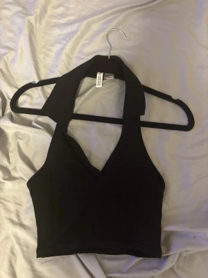 Svart crop topp - Säljer en svart crop topp från H&M. Toppen har en  krage och djup v-ringning framtill, är ärmlös och är backless bakom.