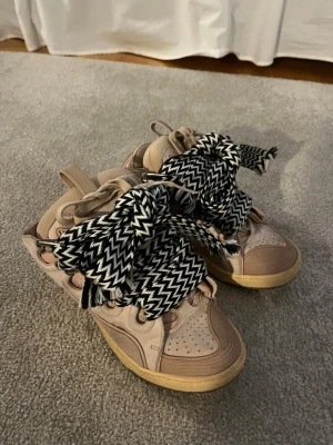 Lanvin curb sneakers med zigzag-snören - Snygga Lanvin Curb sneakers i mycket bra skick. Unika beige sneakers med chunky siluett och tjock sula . Skorna har breda och stora svartvita zigzag-mönstrade skosnören. Perfekta för dig som vill sticka ut med din stil.