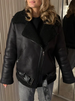 Svart skinnjacka med bälte - Hej!🌸Säljer en snygg svart fake-skinnjacka med bred krage i fuskpäls, dragkedja i sned modell och två fickor med dragkedja. Jackan har ett brett bälte i midjan och detaljer i svart metall. Perfekt oversized look för en trendig stil.  Det förekommer vissa defekter på jackan (ex på bilderna) men den är i helhet väldigt fin🫶