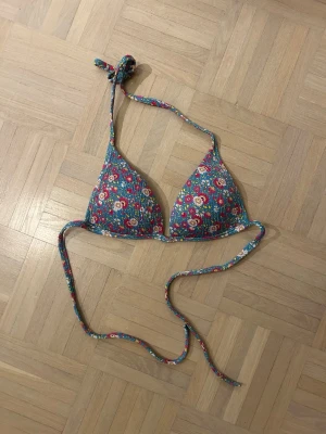 Blommig trekantsbikini topp calzedonia - Söt trekantsbikini med blommigt mönster i blått, rosa, rött och grönt. Bikinin har knyt i nacken och ryggen för justerbar passform. Insidan är blå och materialet känns som syntet, perfekt för strandhäng eller poolen.