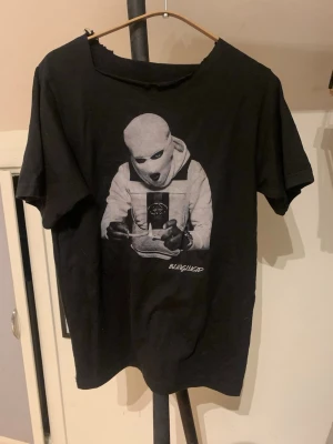 Svart t-shirt med grafiskt tryck - Cool svart t-shirt med ett stort grafiskt tryck på framsidan som visar artisten 1 Cuz tröjan har korta ärmar och en klassisk passform tröjan är tyvärr trasig vid halsen därför så är tröjan utsatt till mycket billigt pris. Perfekt för dig som gillar streetwear och unika prints. Hör av dig vid minsta fundering och pris kan diskuteras! 💯
