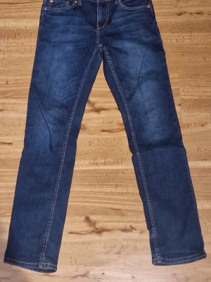 Mörkblå slim jeans från Levi's - Klassiska mörkblå jeans från Levi's med slim fit passform och fem fickor. Jeansen har orange sömmar och en liten röd etikett på bakfickan. Tillverkade i slitstark denim med snygg tvätt och subtila slitningar.