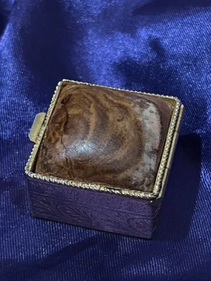 1950s pillerask med någon slags äkta Sten/marmor - 1950s pillerask med någon slags äkta Sten/marmor. En likadan med en ljusare Sten kostar £80 på Etsy.  ”Highlights Vintage from the 1950s Materials: Mamor, Messing Gift wrapping available Translated by Google See in original language This decorative, square Art Deco-style pill box combines classic elegance with refined craftsmanship. The lid is adorned with a smooth marble top, giving each piece a unique appearance. The sides are artfully embossed with floral ornaments, lending the gold-plated br