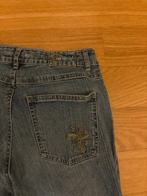 Blå jeans med broderad blomma - Snygga blå jeans från Conard med en broderad blomma i gult på bakfickan. Klassisk femficksmodell med dragkedja och knapp framtill. Jeansen har en lätt tvättad look och är tillverkade i denim.