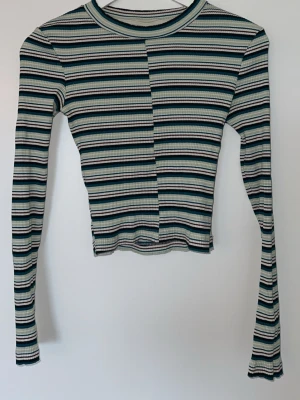 Randig ribbad croppad topp - Trendig långärmad topp med smal ribbad struktur och horisontella ränder i grönt, svart, vitt och beige. Croppad modell med rund halsringning