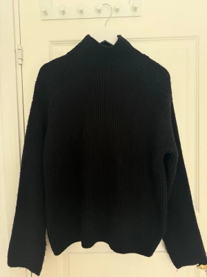 Svart stickad polotröja - En svart stickat tjocktröja med slits vid ärmarna. I tjockt, mjukt och värmande material. 